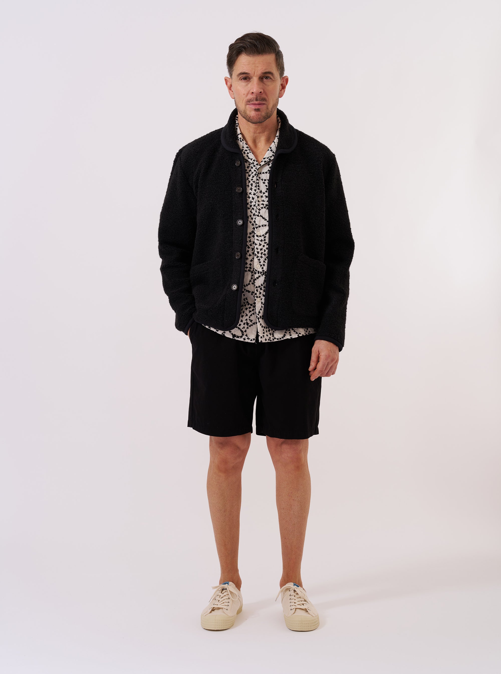 The Black Alvar Fleece Lancaster Jacket is shown as a flat lay against a plain white background. The jacket features a textured black fleece fabric, a rounded shawl collar, and a five-button front closure. Two large patch pockets are visible at the waist, and a smaller patch pocket is located on the chest.
