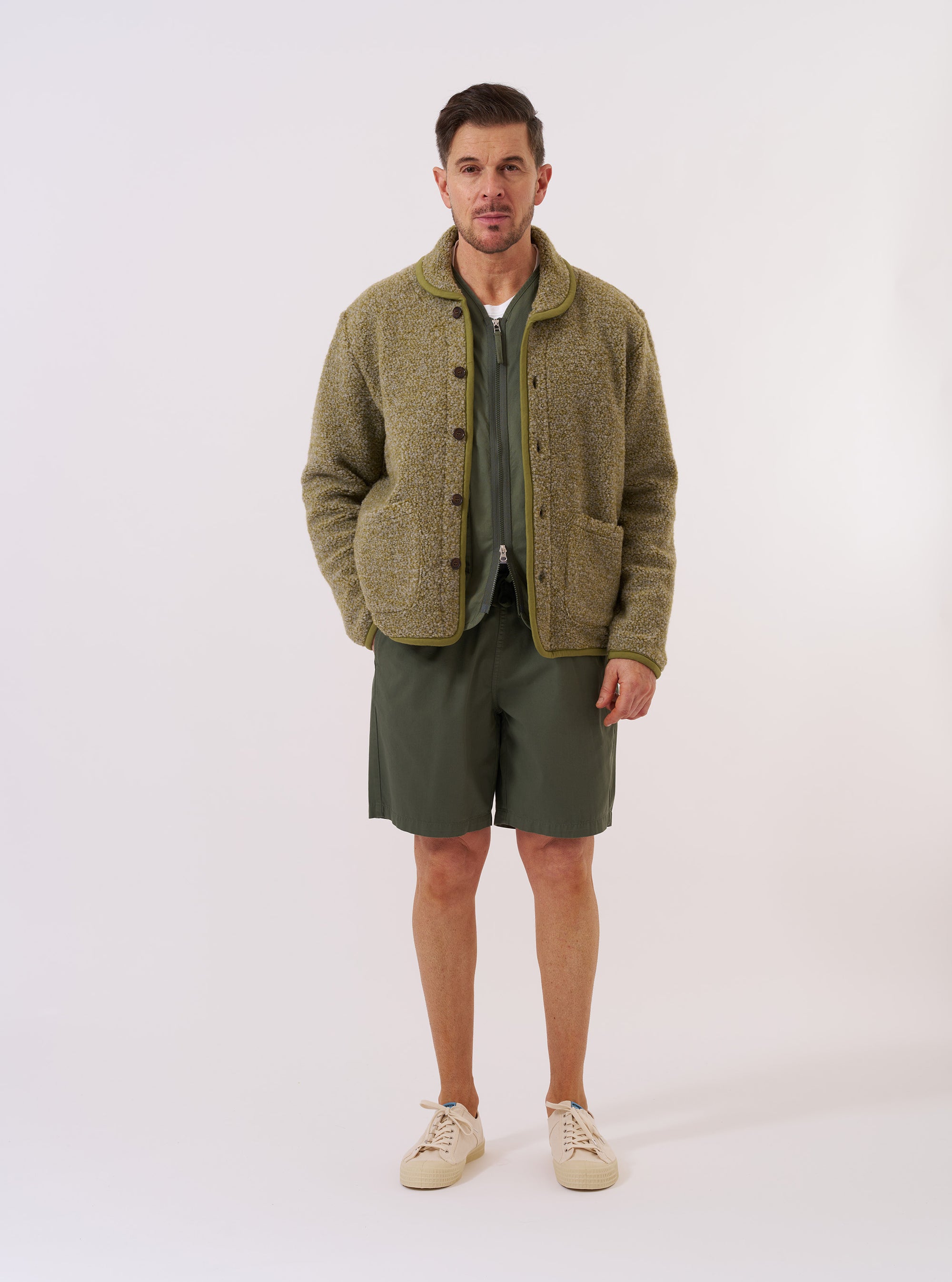The Light Olive Alvar Fleece Lancaster Jacket is shown as a flat lay against a plain white background. The jacket features a curved shawl collar, a six-button front closure, and two large patch pockets at the waist. The garment is made from a textured light olive green fleece with tonal binding along the edges and a curved hem.