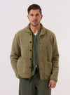 A model wears the Light Olive Alvar Fleece Lancaster Jacket against a plain white background. The jacket features a rounded shawl collar, a six-button front closure, and two large patch pockets at the waist. The light olive fabric has a soft, textured fleece appearance. The model is wearing the jacket layered over a light-colored long-sleeved shirt and dark trousers.