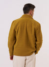 The Yellow Alvar Fleece Lancaster Jacket is worn by a model against a plain white background. The jacket features a rounded collar, a six-button front closure, and two large patch pockets at the hip. The fleece fabric has a textured, yellow ochre appearance. The model is shown from the back, highlighting the jacket's straight hem and relaxed fit. No mannequin is present in the image.