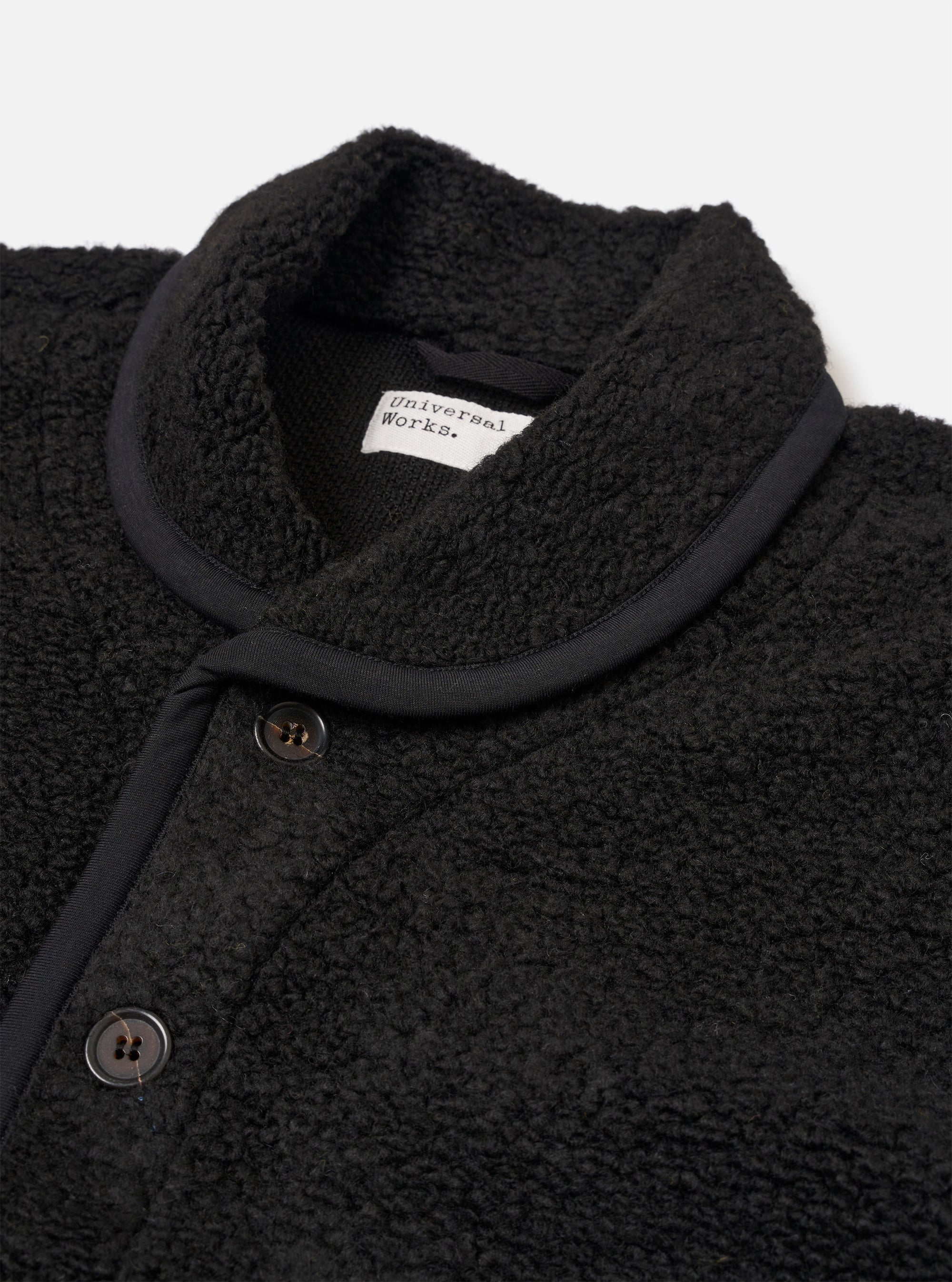 The Black Alvar Fleece Lancaster Jacket is shown as a flat lay against a plain white background. The jacket is crafted from a textured black fleece fabric and features a rounded shawl collar, a central button-down front, and large patch pockets at the waist.