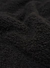 A close-up swatch image of the Black Alvar Fleece Lancaster Jacket highlights the thick, curly, and looped texture of the black fleece fabric. The material fills the entire frame, providing a detailed view of the garment's color and construction.