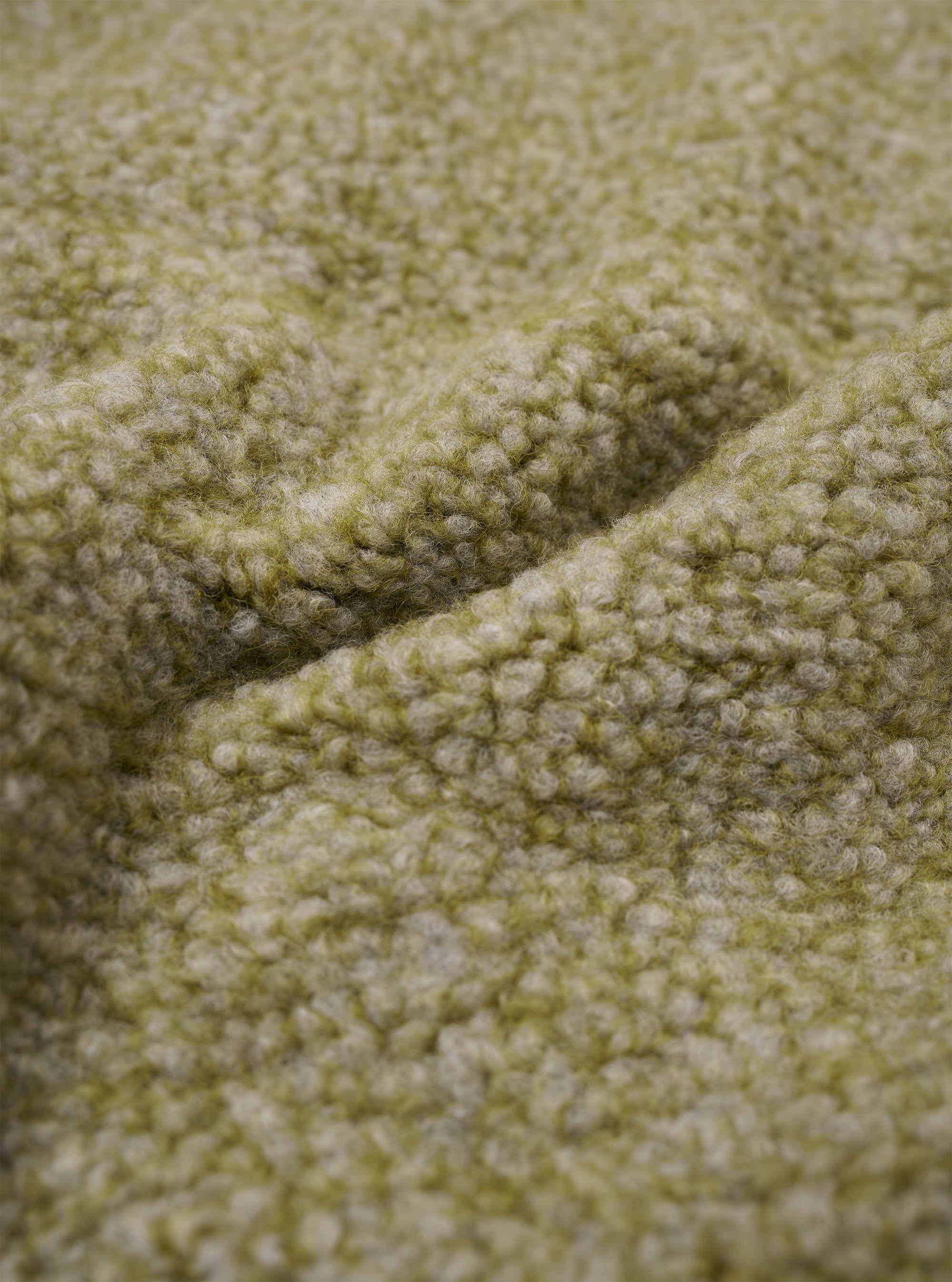 A close-up fabric swatch of the Light Olive Alvar Fleece Lancaster Gilet highlights the thick, curly texture of the light olive green fleece material. The textured wool-blend fabric fills the frame, providing a detailed view of the garment's color and looped weave.