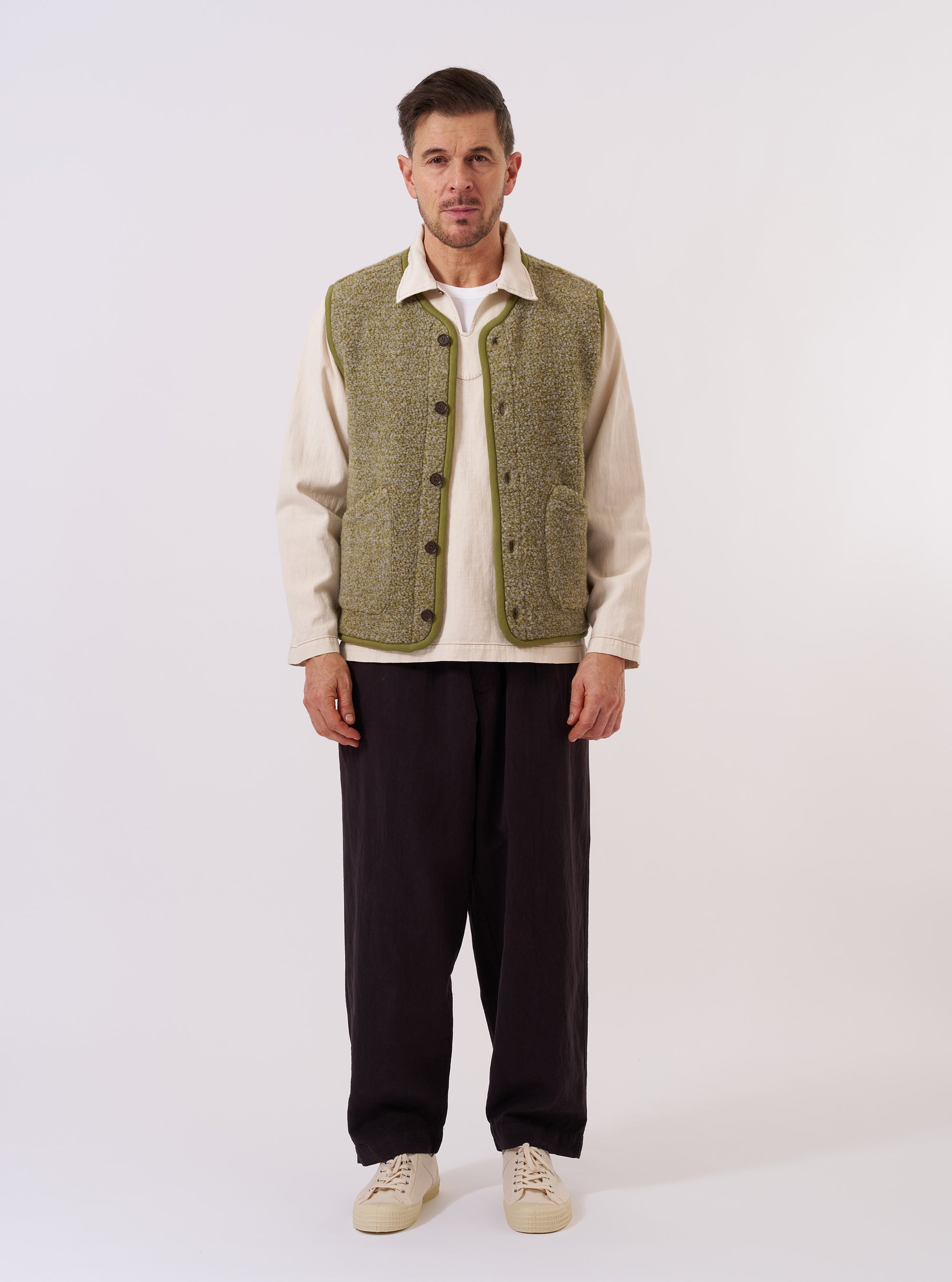 The Light Olive Alvar Fleece Lancaster Gilet is shown as a flat lay against a plain white background. The gilet features a textured, curly fleece fabric in a light olive green, a curved shawl collar, and a six-button front closure. Two large patch pockets are visible at the waist, and the edges of the garment are finished with tonal jersey binding.