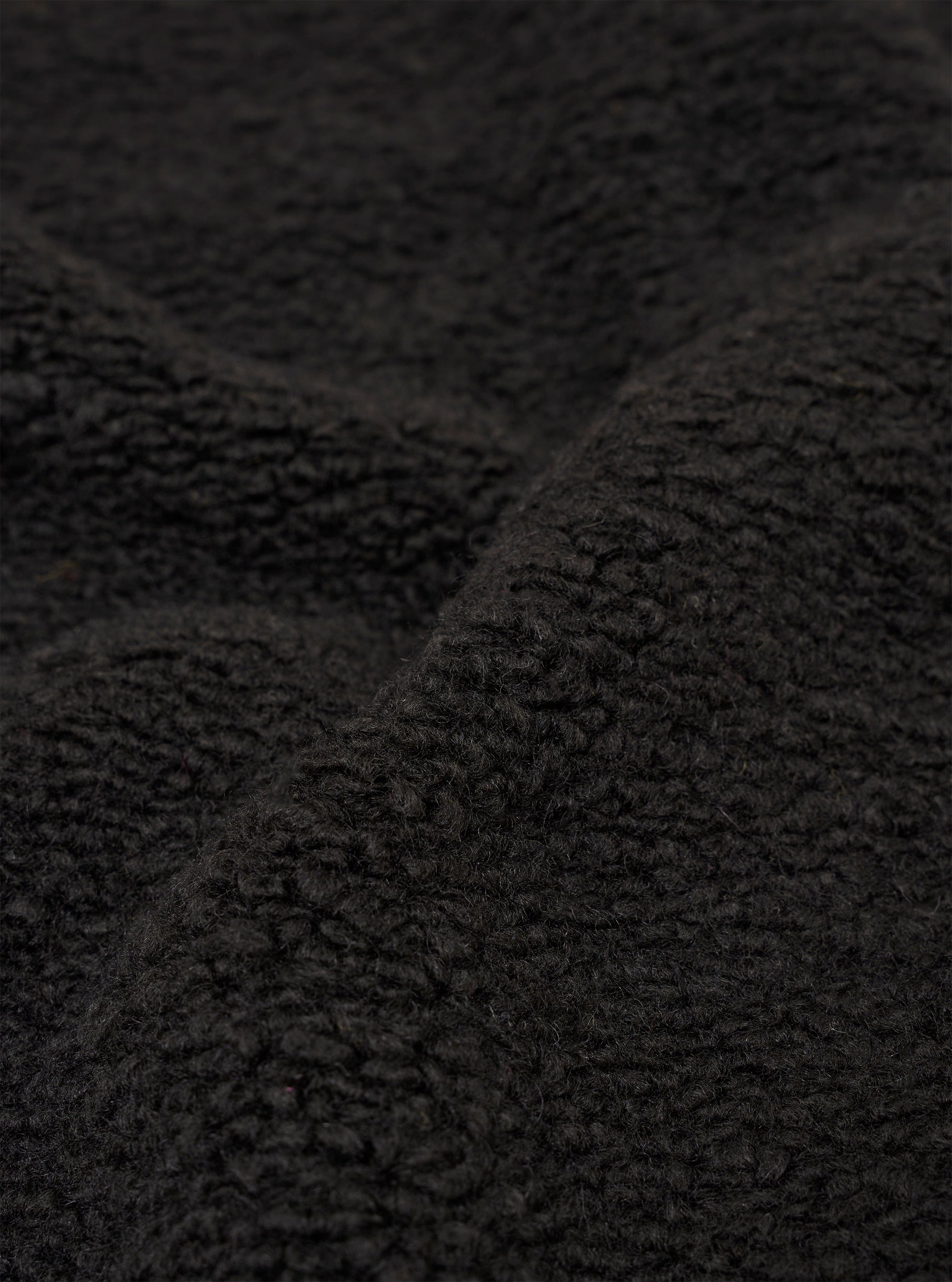 A close-up fabric swatch of the Black Alvar Fleece Lancaster Gilet highlights the thick and curly texture of the black fleece material.