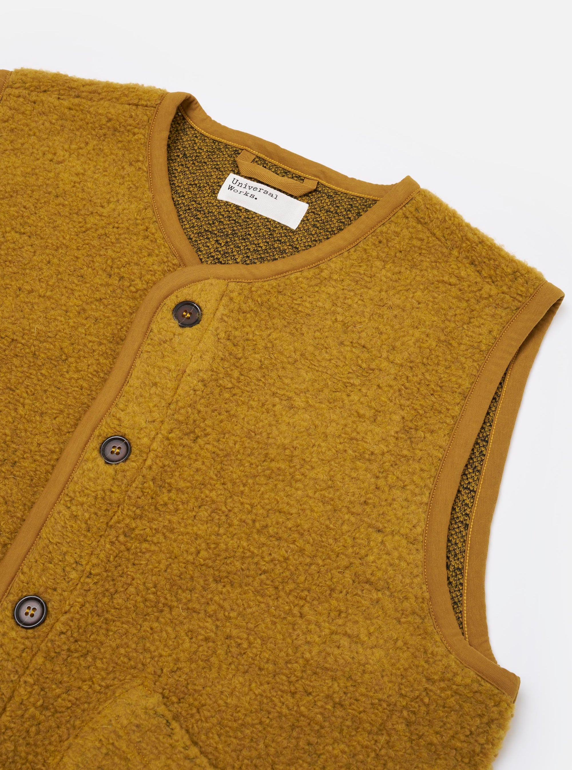 The Yellow Alvar Fleece Lancaster Gilet is shown from the back as a flat lay against a plain white background. The image highlights the textured, looped weave of the yellow/ochre fleece fabric and the simple tonal jersey binding along the armholes and hem.