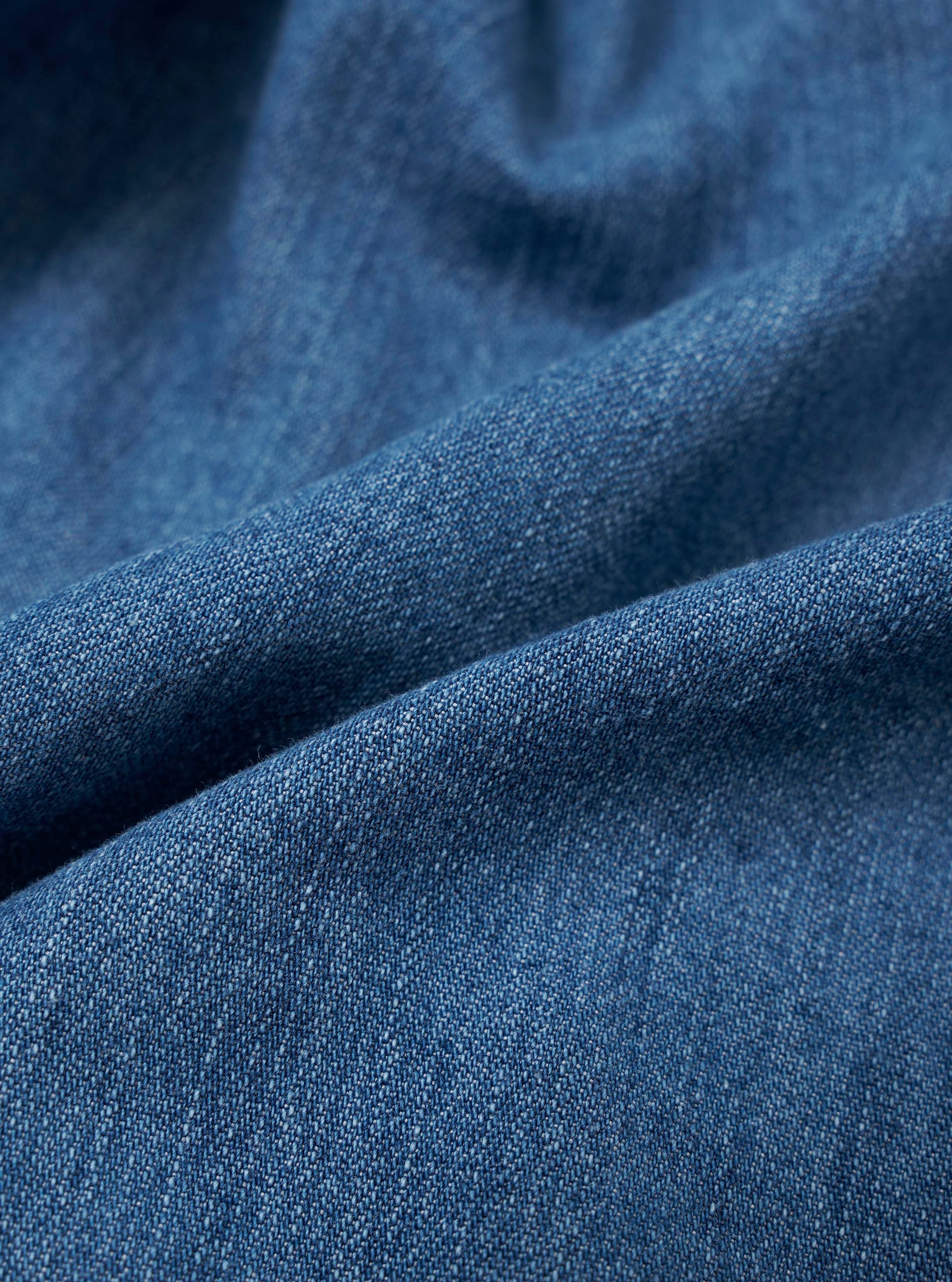 A close-up swatch of the Washed Indigo 8oz Slub Denim Dutch Pant highlights the deep indigo blue color and the highly textured slub finish. The image provides a detailed view of the vintage-like, broken texture and visible grain of the 8oz recycled cotton denim.