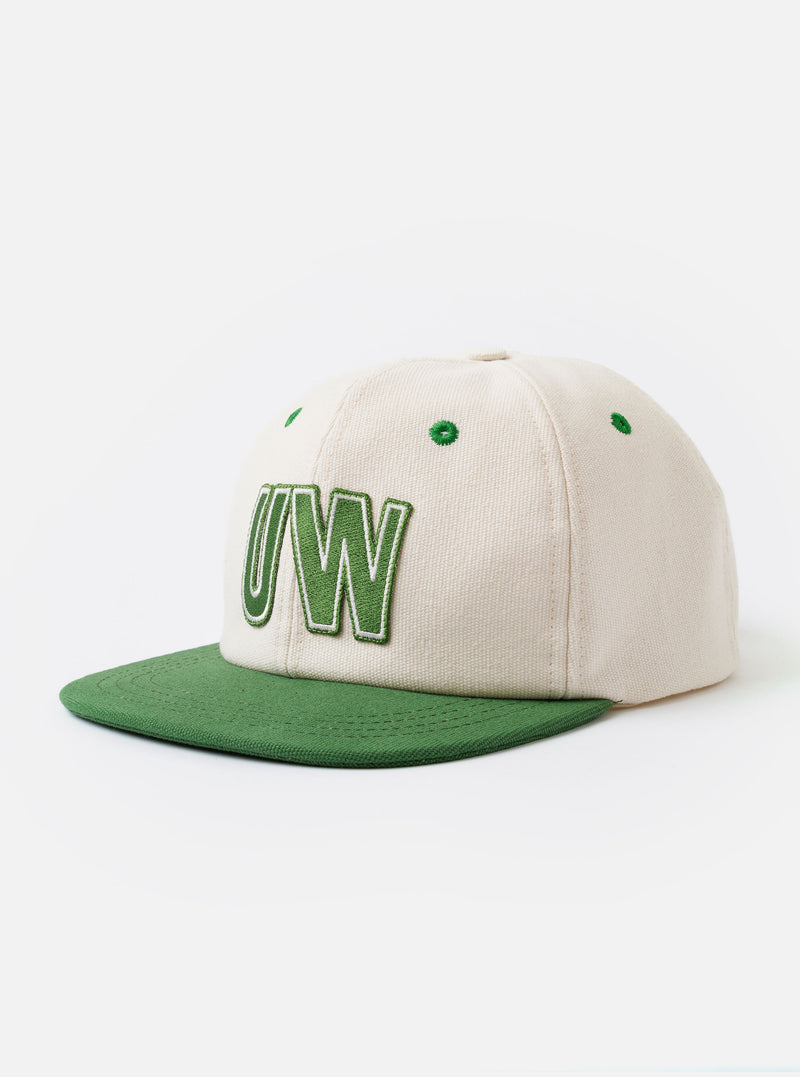 The Ecru/Green Canvas Baseball Hat is shown as a flat lay against a plain white background. The hat features a dual-tone design with an ecru crown and a contrasting green curved brim. A small, circular ventilation eyelet is visible on the side of the crown, and a matching green top button completes the design.
