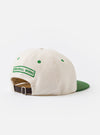 The Ecru/Green Canvas Baseball Hat is displayed from the side as a flat lay against a white background. The cap features a light ecru canvas body with a contrasting dark green curved brim. A prominent green and red striped web detail runs horizontally along the side of the crown.