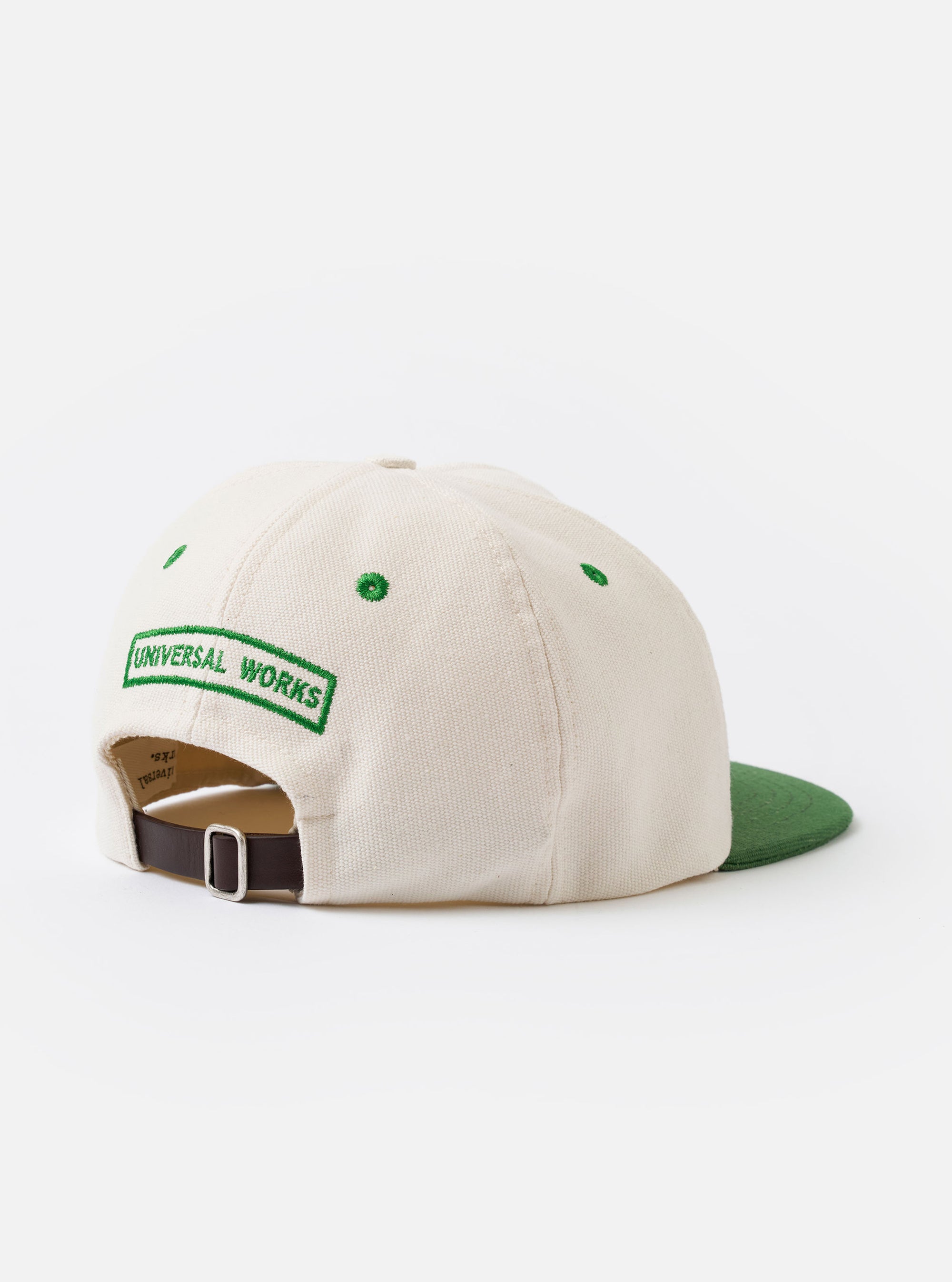 The Ecru/Green Canvas Baseball Hat is displayed from the side as a flat lay against a white background. The cap features a light ecru canvas body with a contrasting dark green curved brim. A prominent green and red striped web detail runs horizontally along the side of the crown.