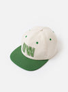 The Ecru/Green Canvas Baseball Hat is shown as a flat lay against a white background. The image displays the rear of the hat, highlighting the adjustable fabric strap and a silver-tone metal buckle. The hat is made from an ecru-colored canvas fabric with green stitching details around the eyelets and seams.