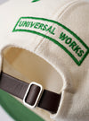 The Ecru/Green Canvas Baseball Hat is shown from a rear three-quarter angle as a flat lay against a plain white background. The image highlights the adjustable fabric strap with a metal buckle and the structured six-panel construction. The hat is made from an ecru cotton canvas with a green brim and matching green top button.