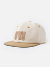 The Ecru/Sand Canvas Baseball Hat is shown as a flat lay against a plain white background. The hat features a six-panel construction in an ecru-colored canvas with a contrasting sand-colored curved peak. It includes a button at the top and visible embroidered eyelets on each panel.