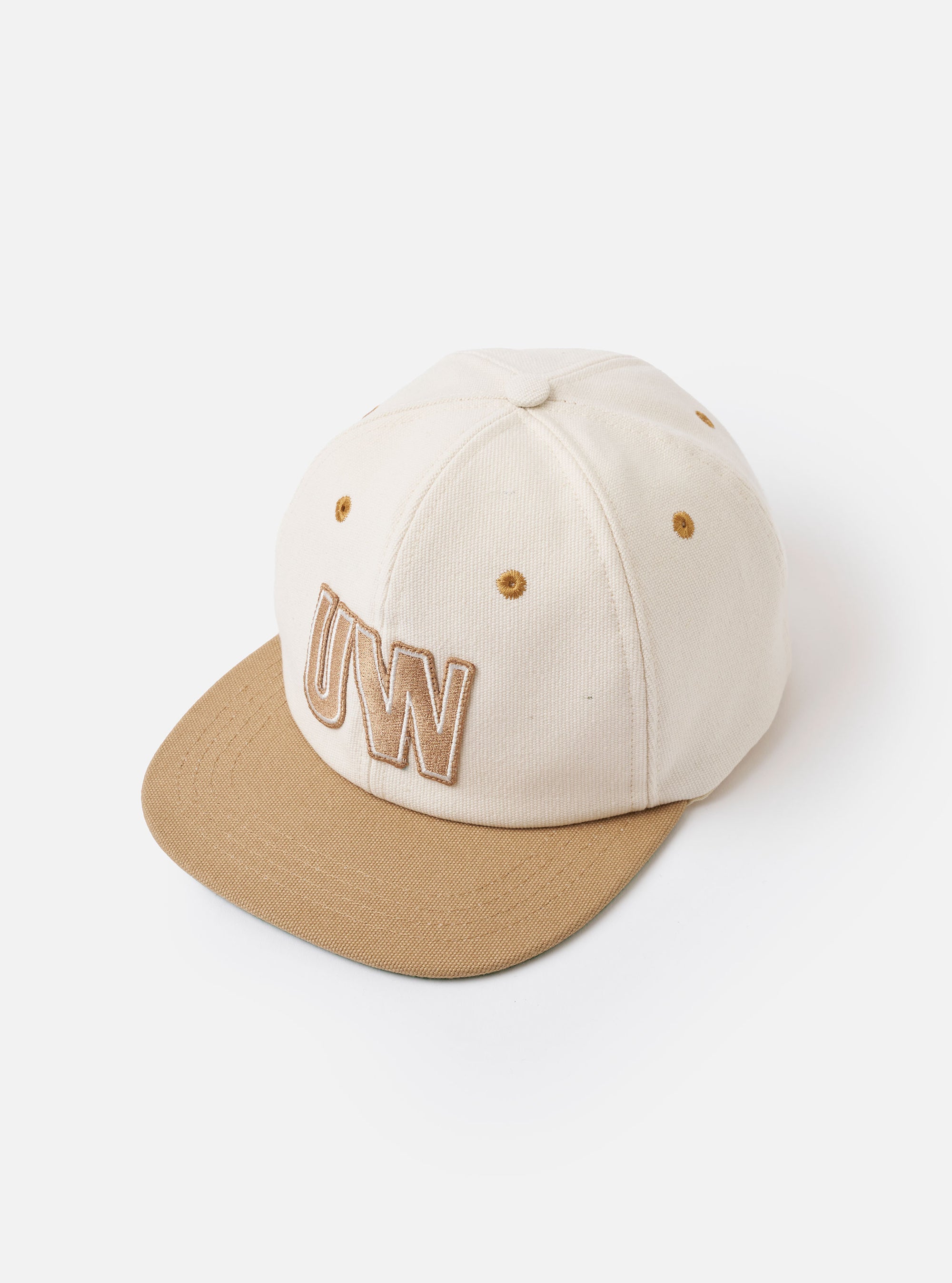 The Ecru/Sand Canvas Baseball Hat is shown as a flat lay against a plain white background. The hat features a classic six-panel crown in an ecru shade with a contrasting sand-colored curved brim. Details include tonal embroidered eyelets for ventilation and a matching fabric-covered button at the top. The canvas material has a visible, durable texture.