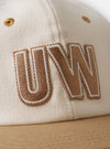 The Ecru/Sand Canvas Baseball Hat is shown in a detail view as a flat lay against a plain white background. The image highlights the adjustable fabric strap at the back with a metal slider and the clean stitching of the six-panel construction. The interior shows a tonal ecru lining and a woven brand label.