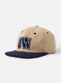 The Sand/Navy Canvas Baseball Hat is shown against a plain white background. The cap features a six-panel construction with a sand-colored crown and a contrasting navy blue curved brim. The design includes embroidered ventilation eyelets and a top button, all crafted from a durable canvas fabric.