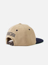 The Sand/Navy Canvas Baseball Hat is shown from a side profile as a flat lay against a plain white background. The hat features a sand-colored crown made from durable cotton canvas and a contrasting navy blue brim. The image highlights the structured six-panel construction and the curved peak.