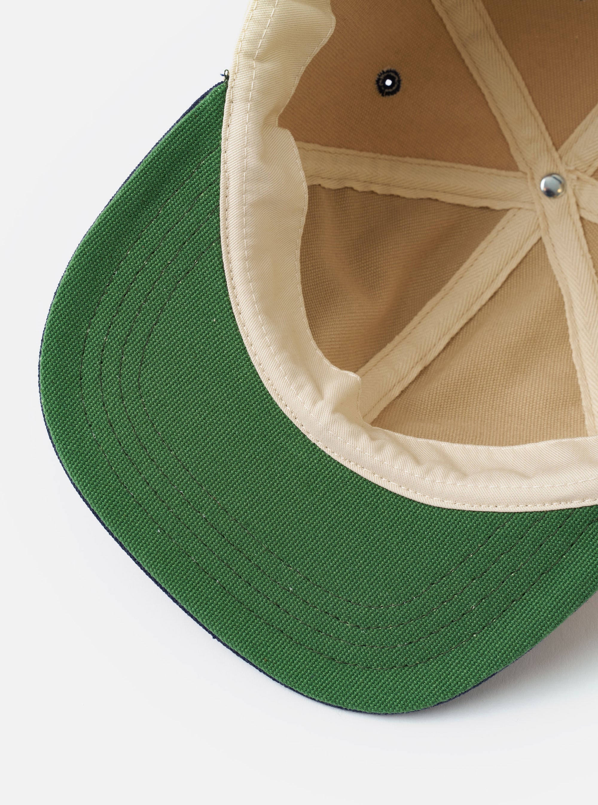 The Sand/Navy Canvas Baseball Hat is shown from the back as a flat lay against a plain white background. The hat features a sand-colored canvas crown and a navy blue adjustable strap with a metal buckle. The construction includes visible stitching and embroidered eyelets.