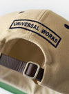 The Sand/Navy Canvas Baseball Hat is shown against a plain white background. The hat features a sand-colored canvas crown and a contrasting navy blue curved brim. It is designed with a classic six-panel construction, a matching top button, and tonal stitched eyelets for ventilation.