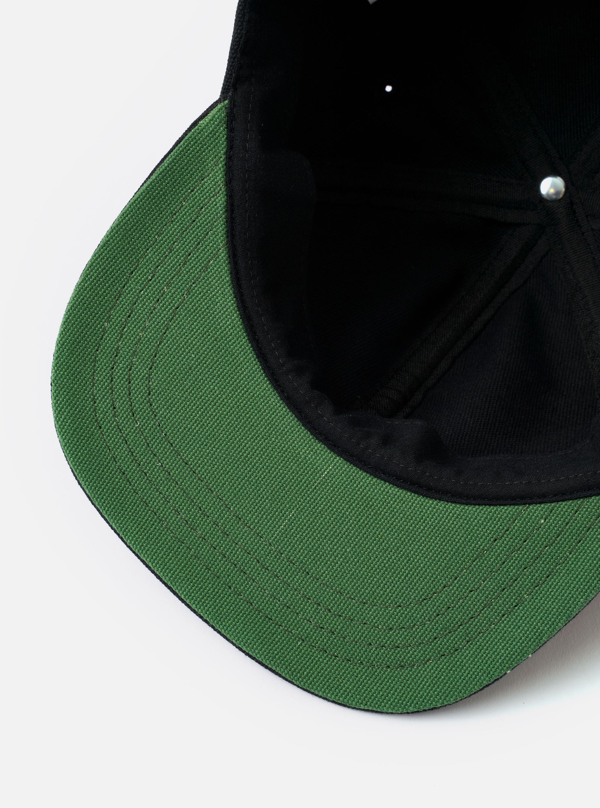 The Black Canvas Baseball Hat is shown from the back as a flat lay against a plain white background. The image highlights the adjustable leather strap with a metal clasp and the six-panel construction of the crown. The fabric is a solid black cotton canvas with visible eyelet details.