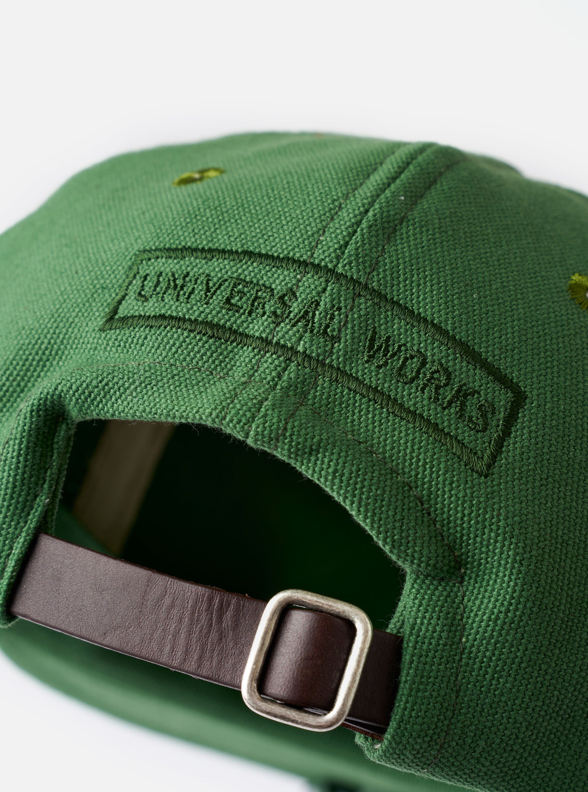 The Green Canvas Baseball Hat is shown in a close-up detail shot against a plain white background. The image highlights the durable texture of the green cotton canvas fabric, focusing on the six-panel construction, tonal stitching, and an embroidered ventilation eyelet.