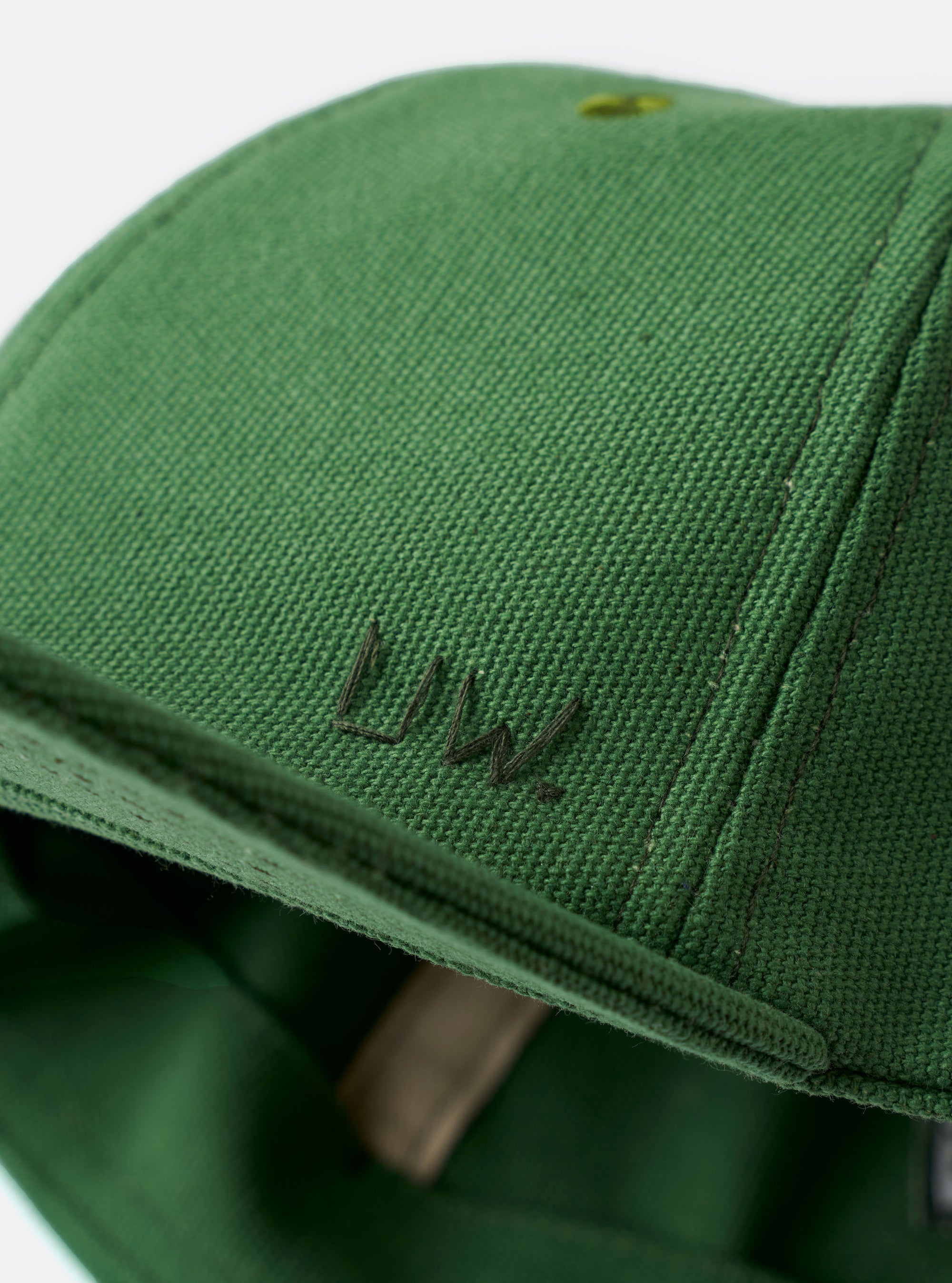 The Green Canvas Baseball Hat is shown from a side angle against a plain white background. The hat features a structured six-panel crown, a curved brim, and tonal embroidered eyelets. The durable green cotton canvas material has a visible texture.