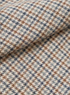 Close-up fabric detail of the Lester Dogtooth Franck Jacket in taupe, showing a woven wool-effect dogtooth pattern in cream, tan brown and slate blue. The fabric is folded to reveal texture and weight. No model or mannequin is present.