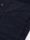 Close-up flat lay of the navy Bob Wool Mix Bakers Overshirt on a white surface, showing a large patch chest pocket with topstitched edges and a dark horn-effect button above. The fabric has a brushed wool-mix texture with a subtle dark navy check pattern.