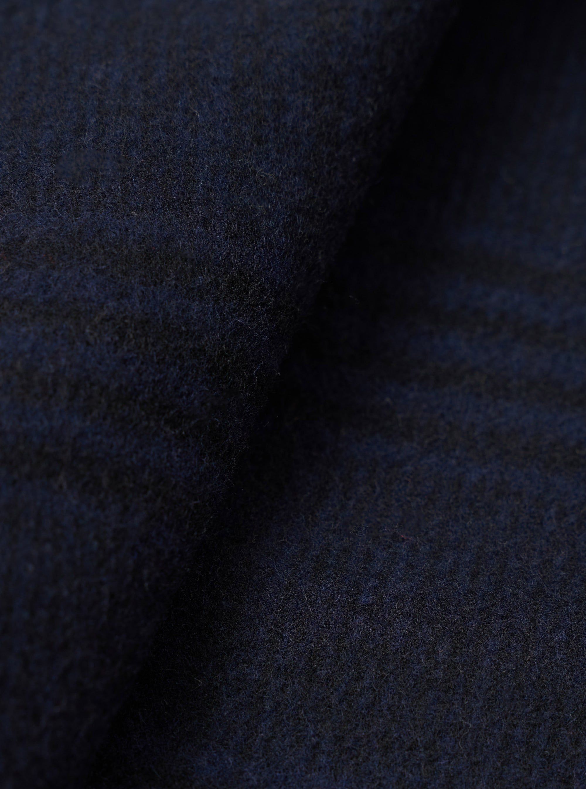 Close-up of the navy wool mix fabric of a bakers overshirt, showing a dense, lightly brushed texture with subtle blue and dark grey tonal variation. The fabric has a soft, boiled-wool-style surface with fine surface fibres visible throughout. No background is visible.