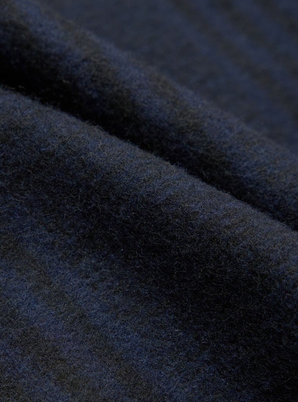 Close-up fabric detail shot of the navy wool mix oxford pant. The brushed, lightly felted textile shows a dense, softly napped surface with fine individual fibres visible throughout. Deep navy tones shift subtly across the folded cloth, revealing slight blue and charcoal variation in the weave.
