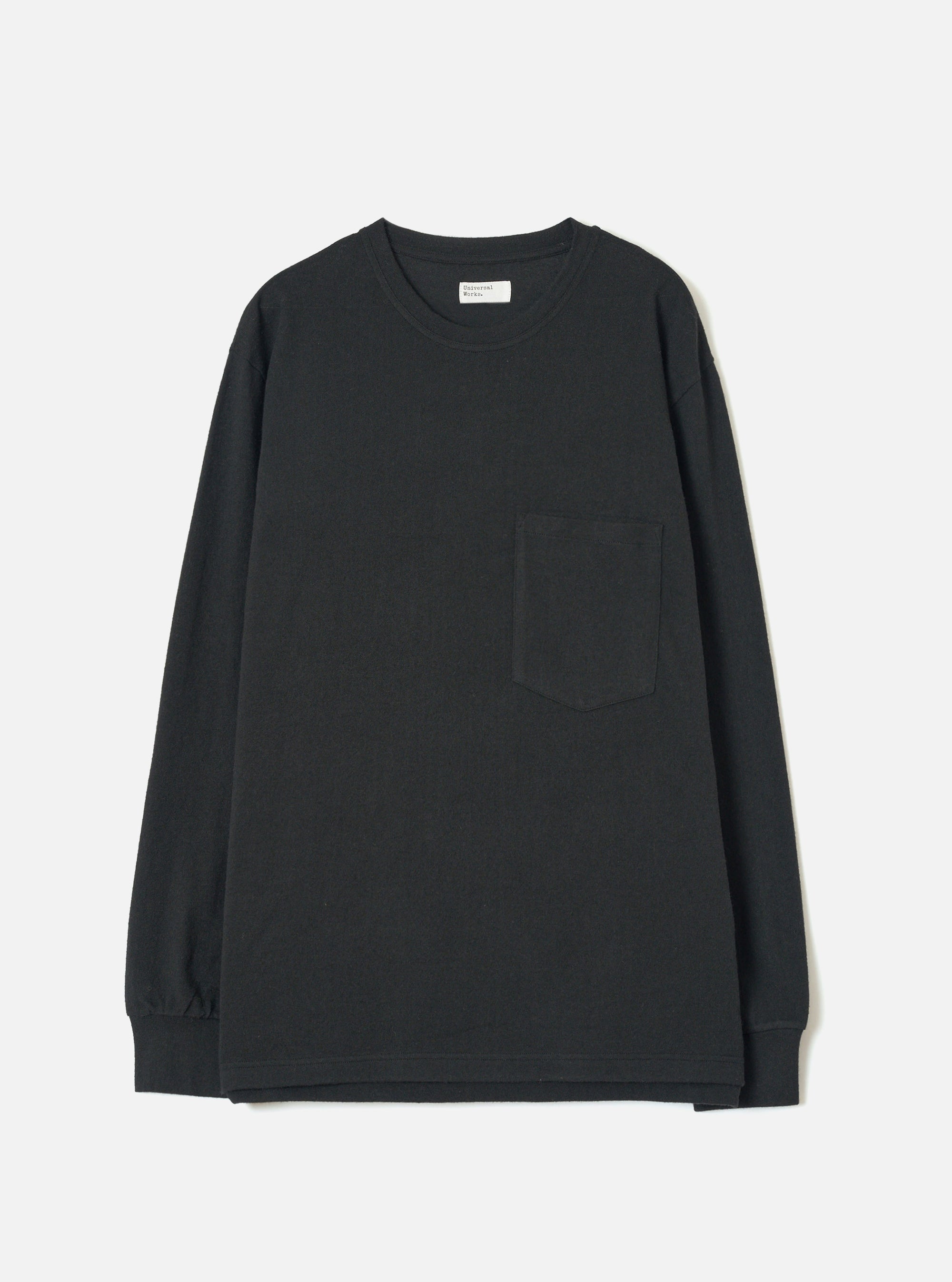 Black long-sleeve pocket tee in a recycled wool mix, laid flat on a light grey studio backdrop. Features a ribbed crew neck with a woven label at the back, a single patch pocket on the left chest, ribbed cuffs, and a plain hem. The jersey fabric has a smooth, mid-weight texture throughout.