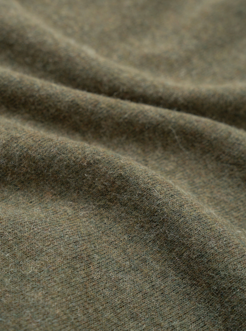 Close-up detail shot of the olive recycled wool mix fabric used in the pocket tee. The mélange knit shows a soft, brushed surface with fine fibres visible across its texture. Gentle folds in the fabric highlight its weight and drape.