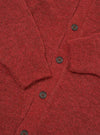 Close-up flat lay of a deep orange alpaca knit cardigan on a white surface. The V-neckline, button placket with four visible dark brown four-hole buttons, a ribbed cuff, and a patch pocket are shown. The marl knit fabric has a soft, fluffy texture with flecks of darker tone throughout.