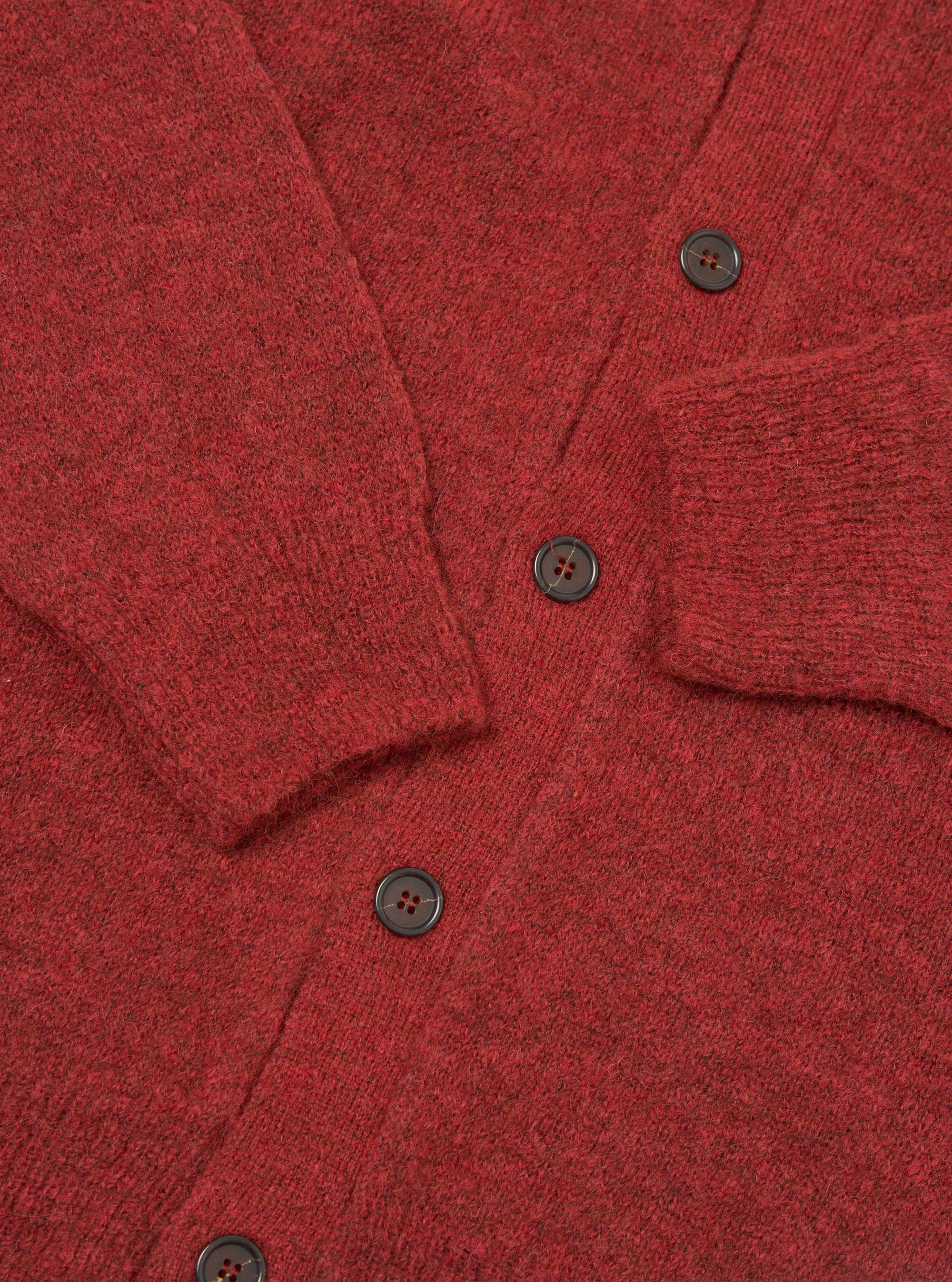 Close-up flat lay of a deep orange alpaca knit cardigan on a white surface. The V-neckline, button placket with four visible dark brown four-hole buttons, a ribbed cuff, and a patch pocket are shown. The marl knit fabric has a soft, fluffy texture with flecks of darker tone throughout.