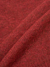 Close-up fabric shot of the deep orange alpaca knit cardigan, showing a folded section of the textile. The marl knit texture is clearly visible, with dark flecks running through the warm red-orange yarn. The soft, slightly hairy surface is characteristic of alpaca fibre. Plain white studio background.