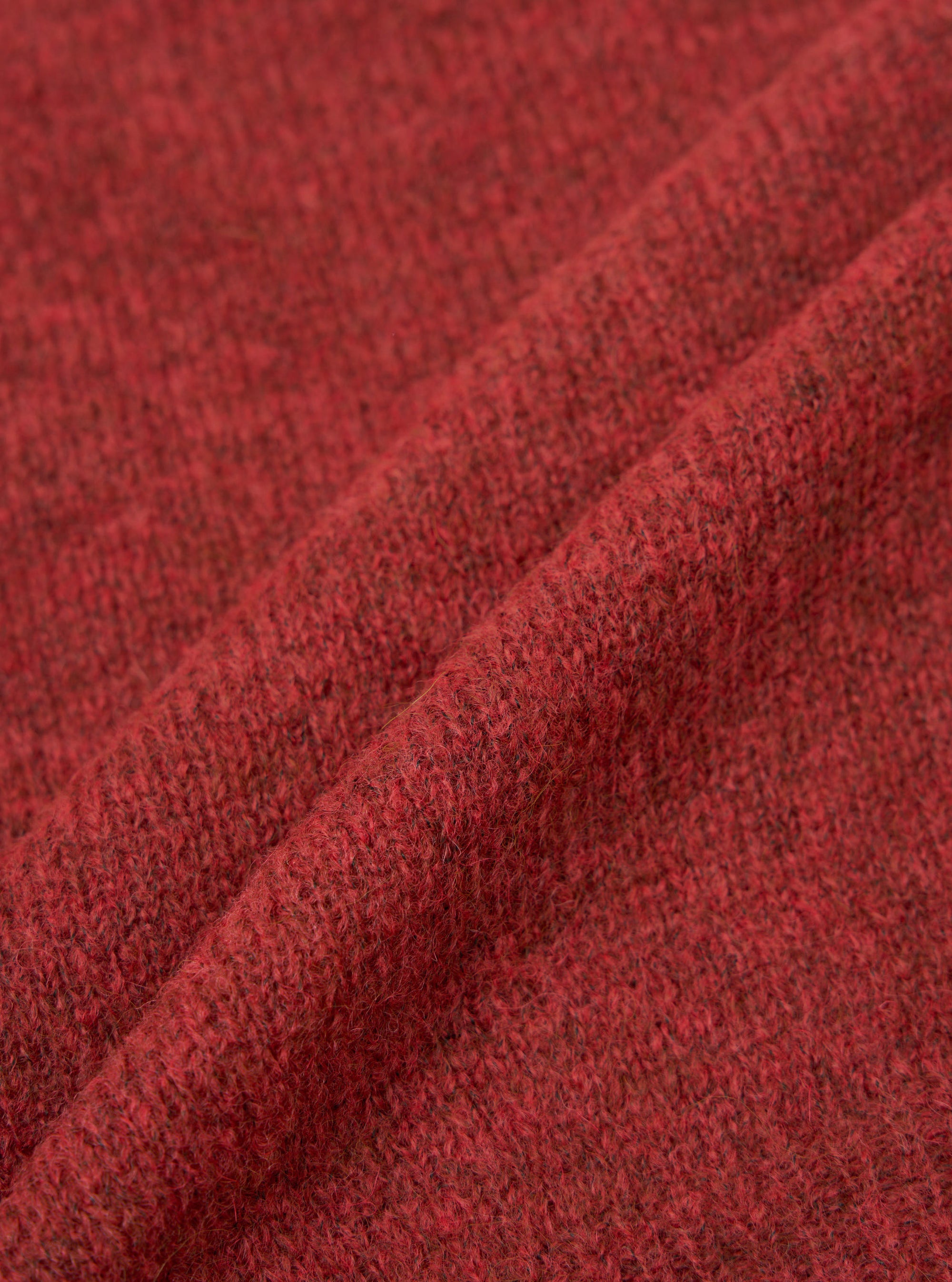 Close-up fabric shot of the deep orange alpaca knit cardigan, showing a folded section of the textile. The marl knit texture is clearly visible, with dark flecks running through the warm red-orange yarn. The soft, slightly hairy surface is characteristic of alpaca fibre. Plain white studio background.