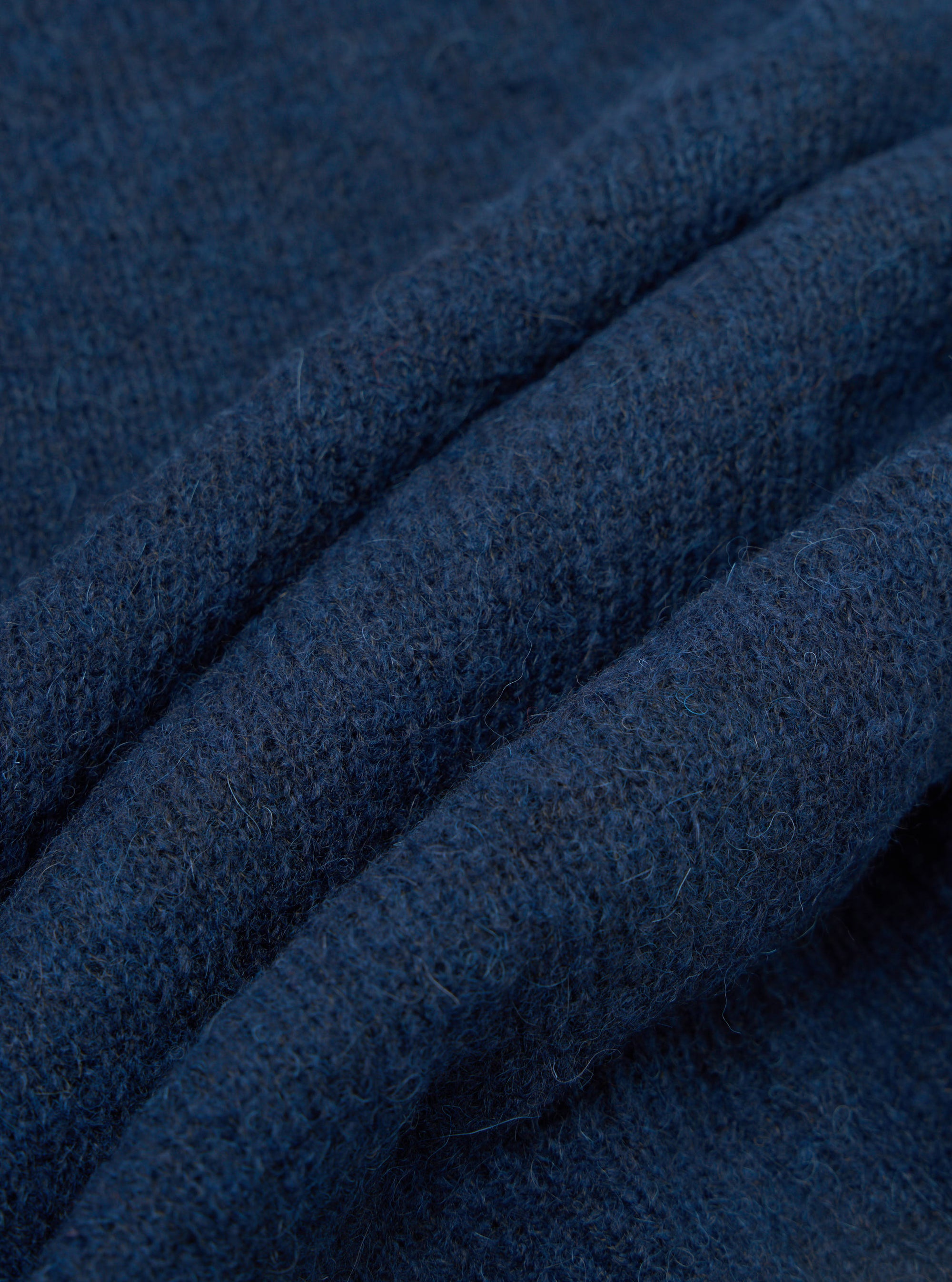 Close-up detail of the navy alpaca knit fabric of the David Cardigan, showing soft, slightly hairy fibres and a textured knit structure. The fabric is gathered into deep folds, highlighting its weight and warmth. Shot against a plain white studio background.