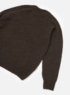 Brown alpaca knit crew neck sweater laid flat on a white studio surface. The shot is cropped to show the back body and one full sleeve. The fabric has a soft, slightly fluffy texture with a marl-effect weave. A ribbed hem and ribbed cuff are visible at the sleeve end.