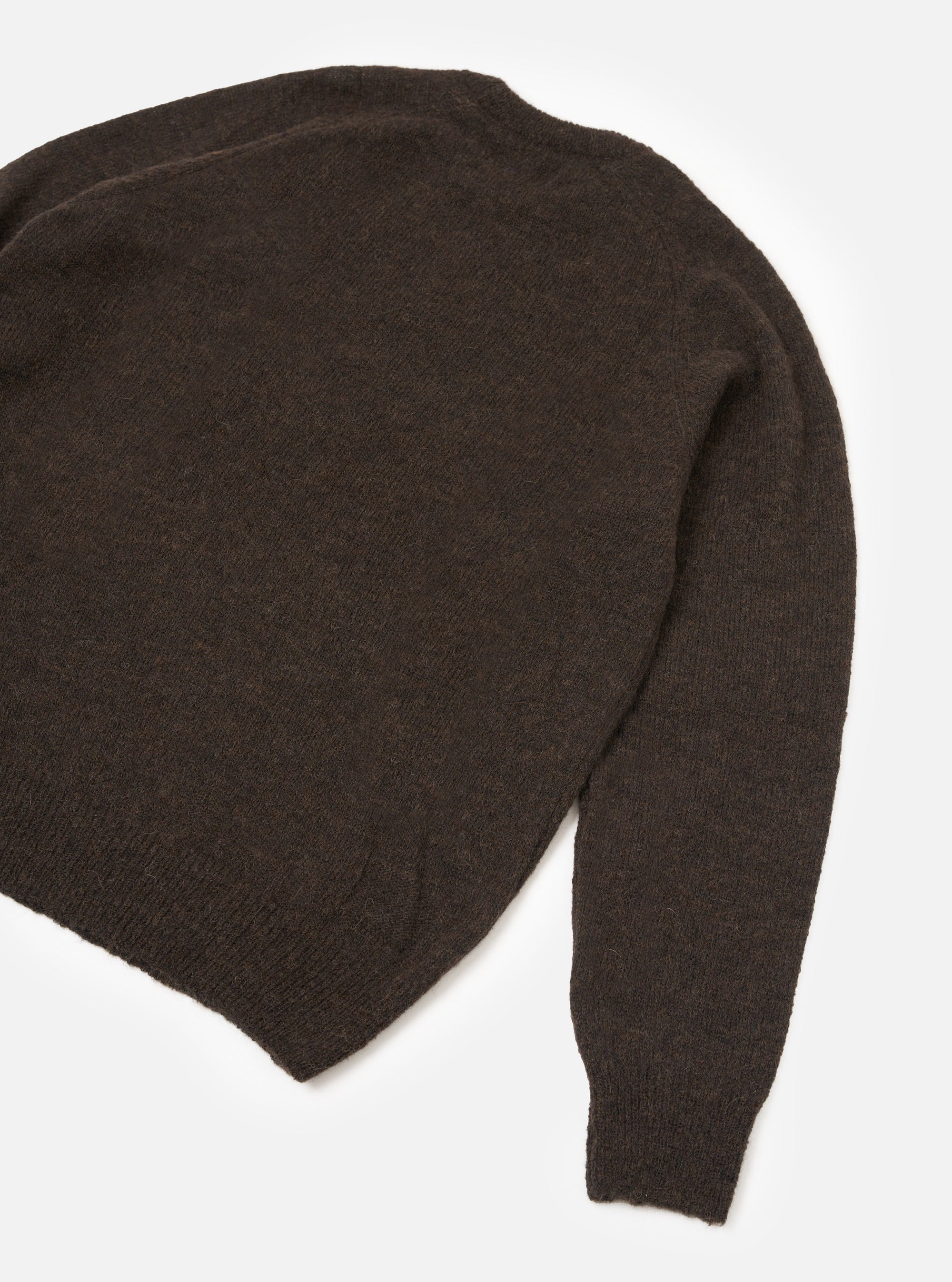 Brown alpaca knit crew neck sweater laid flat on a white studio surface. The shot is cropped to show the back body and one full sleeve. The fabric has a soft, slightly fluffy texture with a marl-effect weave. A ribbed hem and ribbed cuff are visible at the sleeve end.