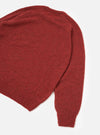 Flat lay of a deep orange alpaca knit crew neck jumper on a white studio backdrop. The shot is cropped to show the upper body and one full sleeve. The fine marl knit fabric has a soft, hairy texture. A ribbed crew neck collar, ribbed hem and ribbed cuff are visible.