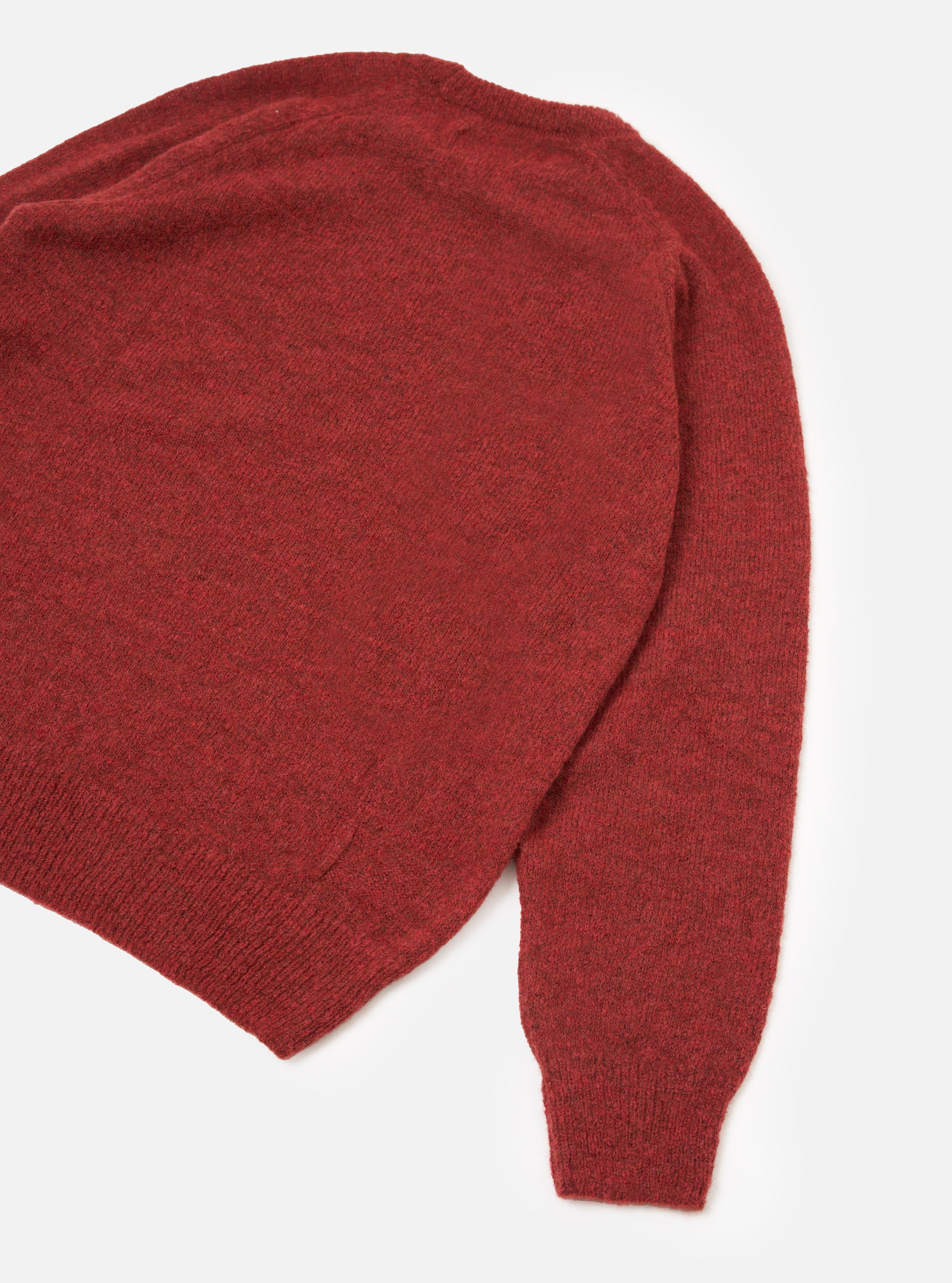 Flat lay of a deep orange alpaca knit crew neck jumper on a white studio backdrop. The shot is cropped to show the upper body and one full sleeve. The fine marl knit fabric has a soft, hairy texture. A ribbed crew neck collar, ribbed hem and ribbed cuff are visible.
