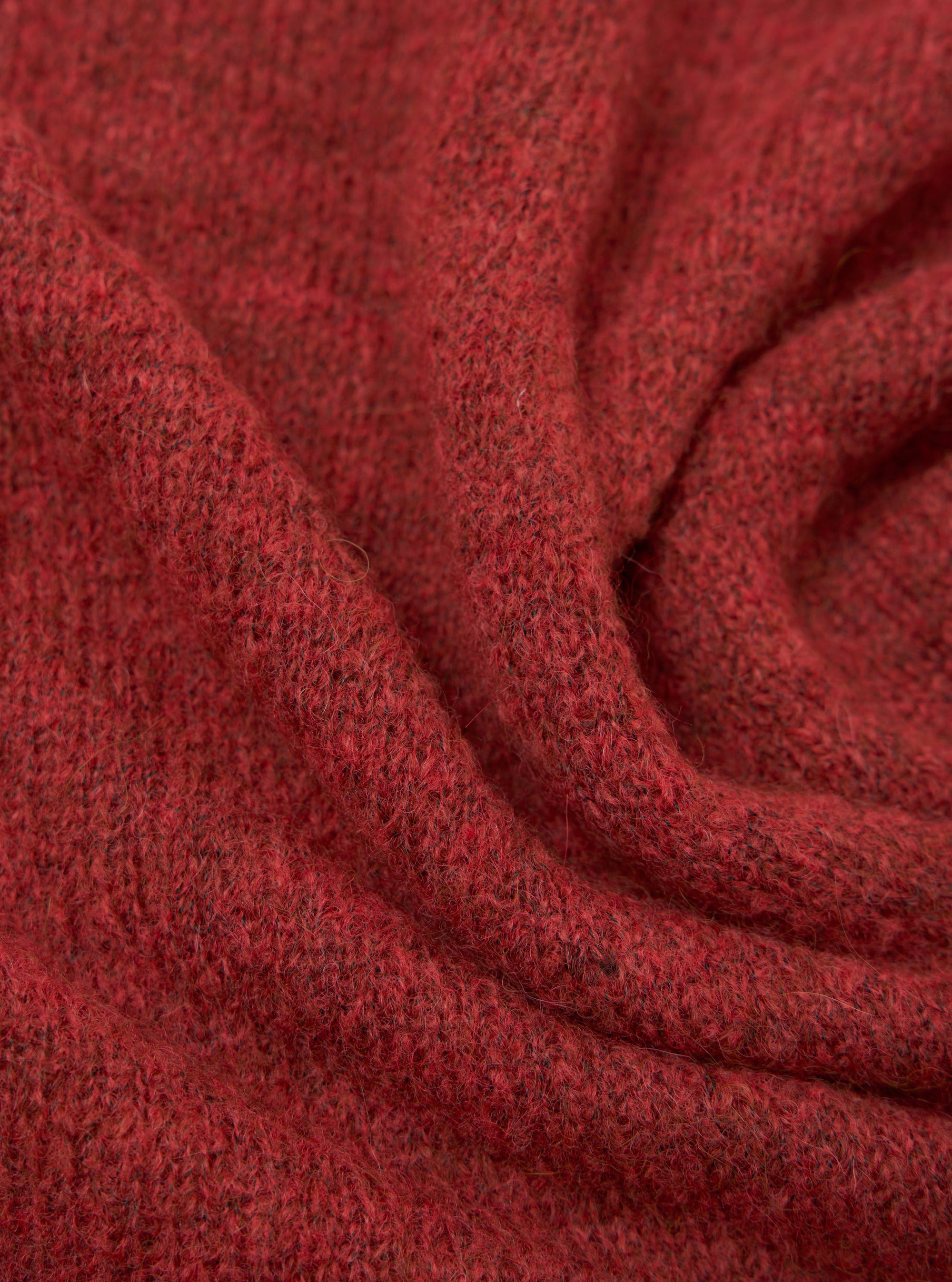 Close-up of the deep orange alpaca knit fabric of the Lyon Crew, showing a soft, fluffy texture with a fine marl knit construction. Dark flecks run throughout the warm red-orange yarn. The fabric is gathered into soft folds, highlighting its weight and drape.