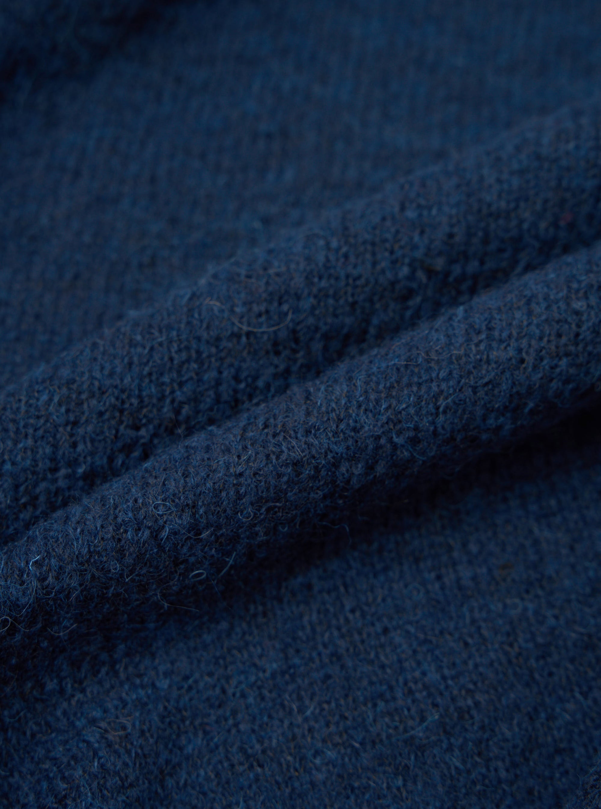 Close-up detail shot of the navy alpaca knit fabric, showing a soft, slightly hairy texture with a fine knit construction. The deep blue-navy yarn has subtle tonal variation. The fabric is loosely folded to show its depth and loft. No background is visible.