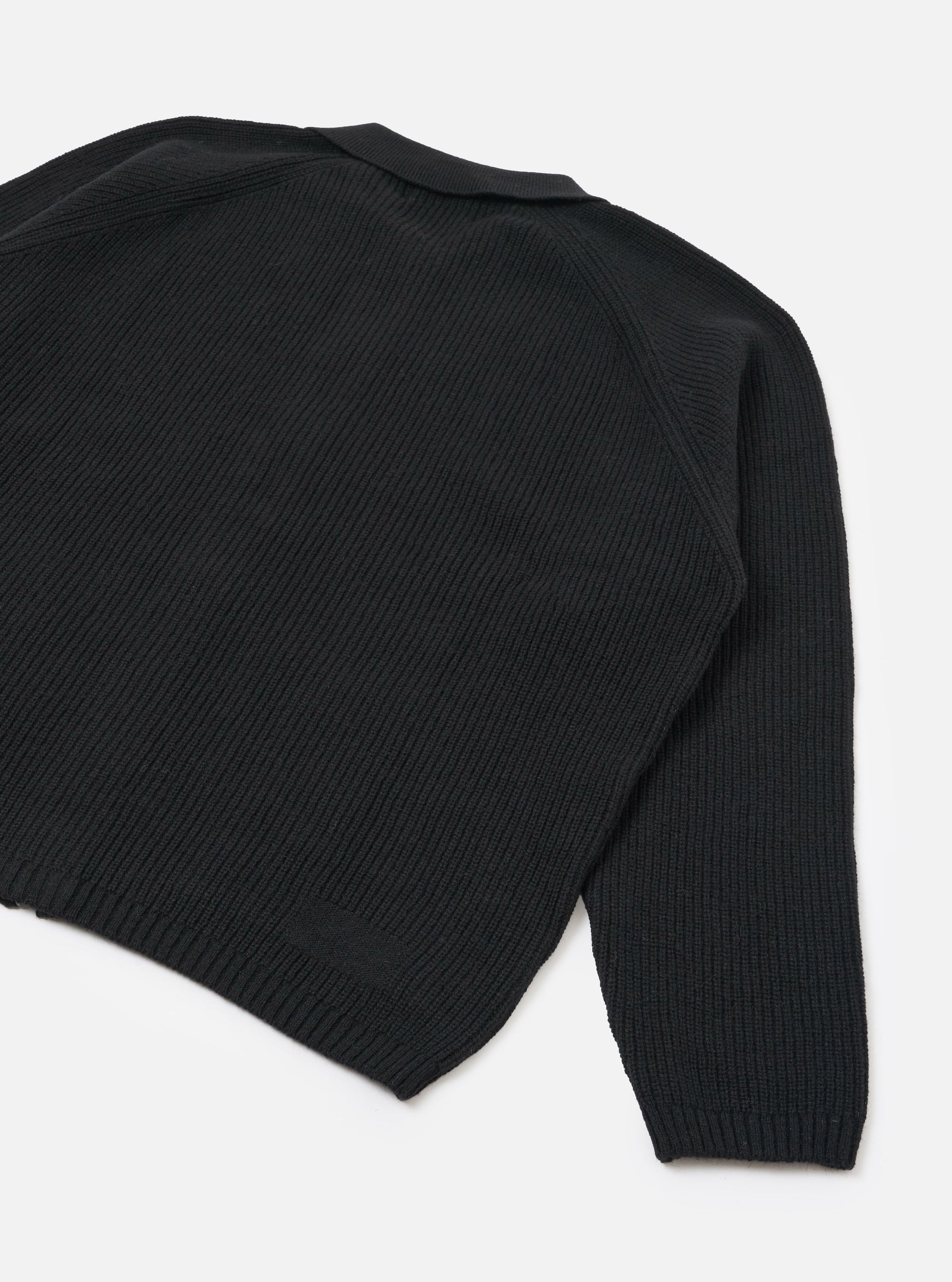 Black ribbed-knit eco wool zip cardigan, flat lay on a white studio backdrop. Close-up rear angle showing the back panel, one full sleeve, and ribbed hem. Chunky vertical rib texture throughout, with a ribbed cuff and a ribbed collar visible at the top edge.