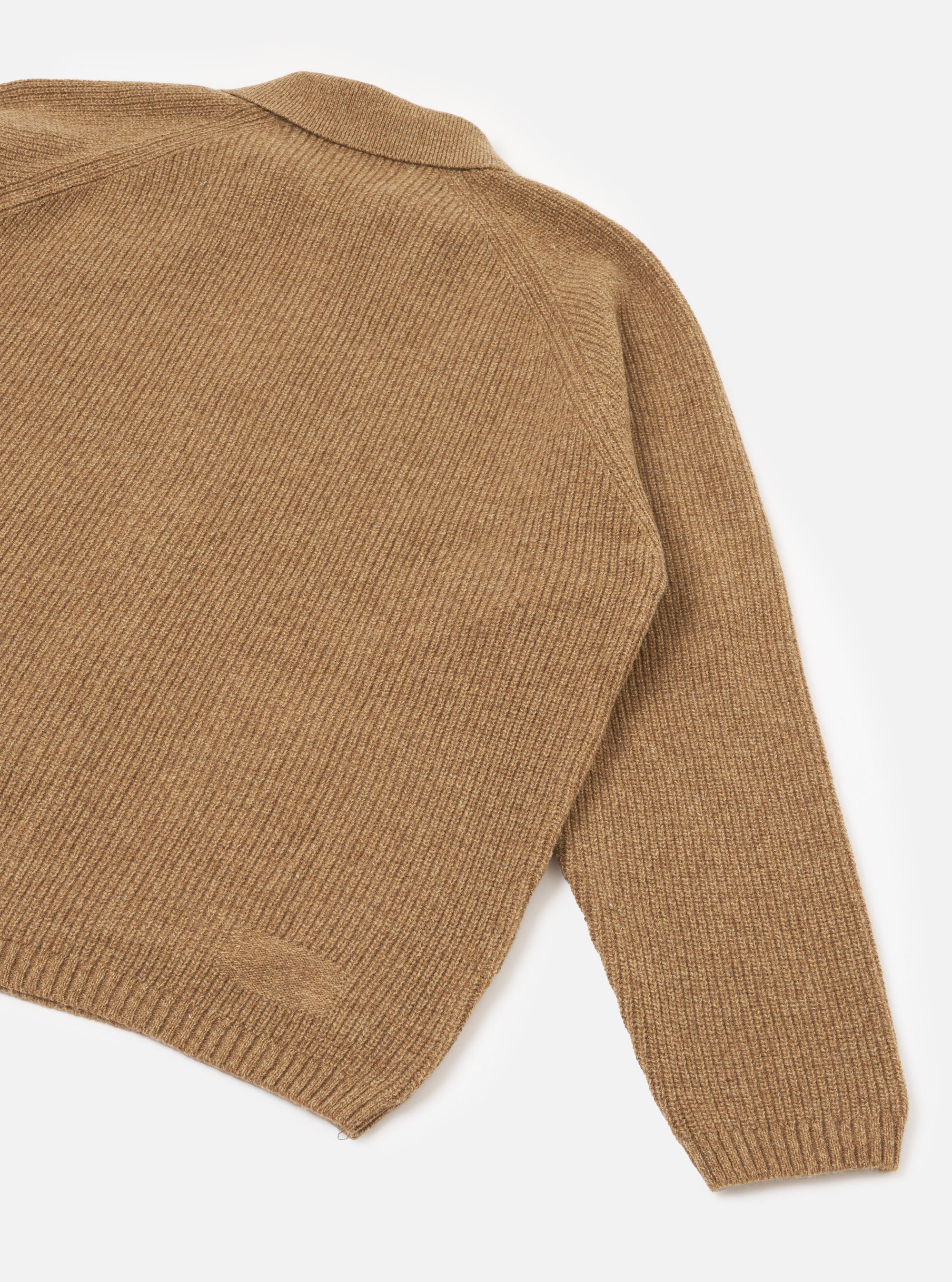 Close-up flat lay of a tawny eco wool zip cardigan on a white studio backdrop. The ribbed knit texture is visible across the body and raglan sleeve. A ribbed cuff and ribbed hem band are shown. A small zip pull is visible at the bottom hem. The spread collar is partially visible at the top.