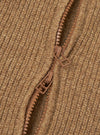 Close-up detail of the tawny eco wool zip cardigan showing a two-way brown zip partially open against chunky ribbed knit fabric. The zip pulls and teeth are tonal brown plastic. The hairy, textured wool-blend rib is visible across the full frame.