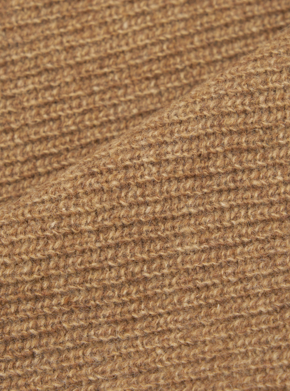 Close-up of the tawny eco wool fabric on the zip cardigan, showing a chunky, open-knit texture with a hairy, brushed finish. The warm camel-brown yarn has visible flecks of darker and lighter tones throughout. A fold in the fabric runs diagonally across the frame.