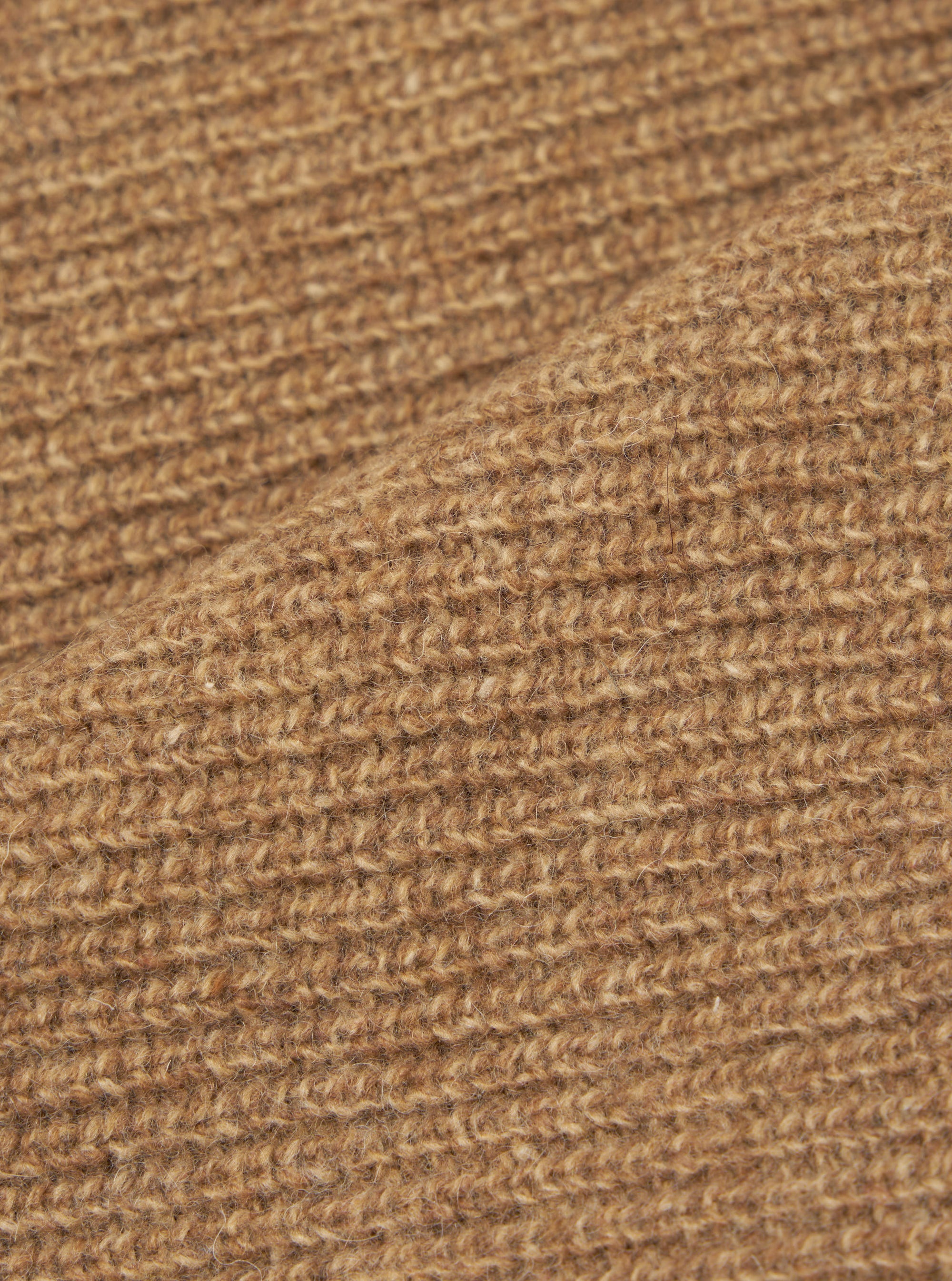 Close-up of the tawny eco wool fabric on the zip cardigan, showing a chunky, open-knit texture with a hairy, brushed finish. The warm camel-brown yarn has visible flecks of darker and lighter tones throughout. A fold in the fabric runs diagonally across the frame.