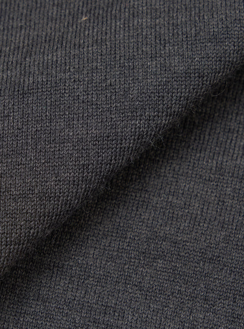 Close-up of the charcoal merino knit fabric, showing a fine, uniform jersey stitch with a soft, slightly textured surface. The dark grey tone has a subtle heathered quality. The fabric is folded to display drape and thickness against a plain white background.