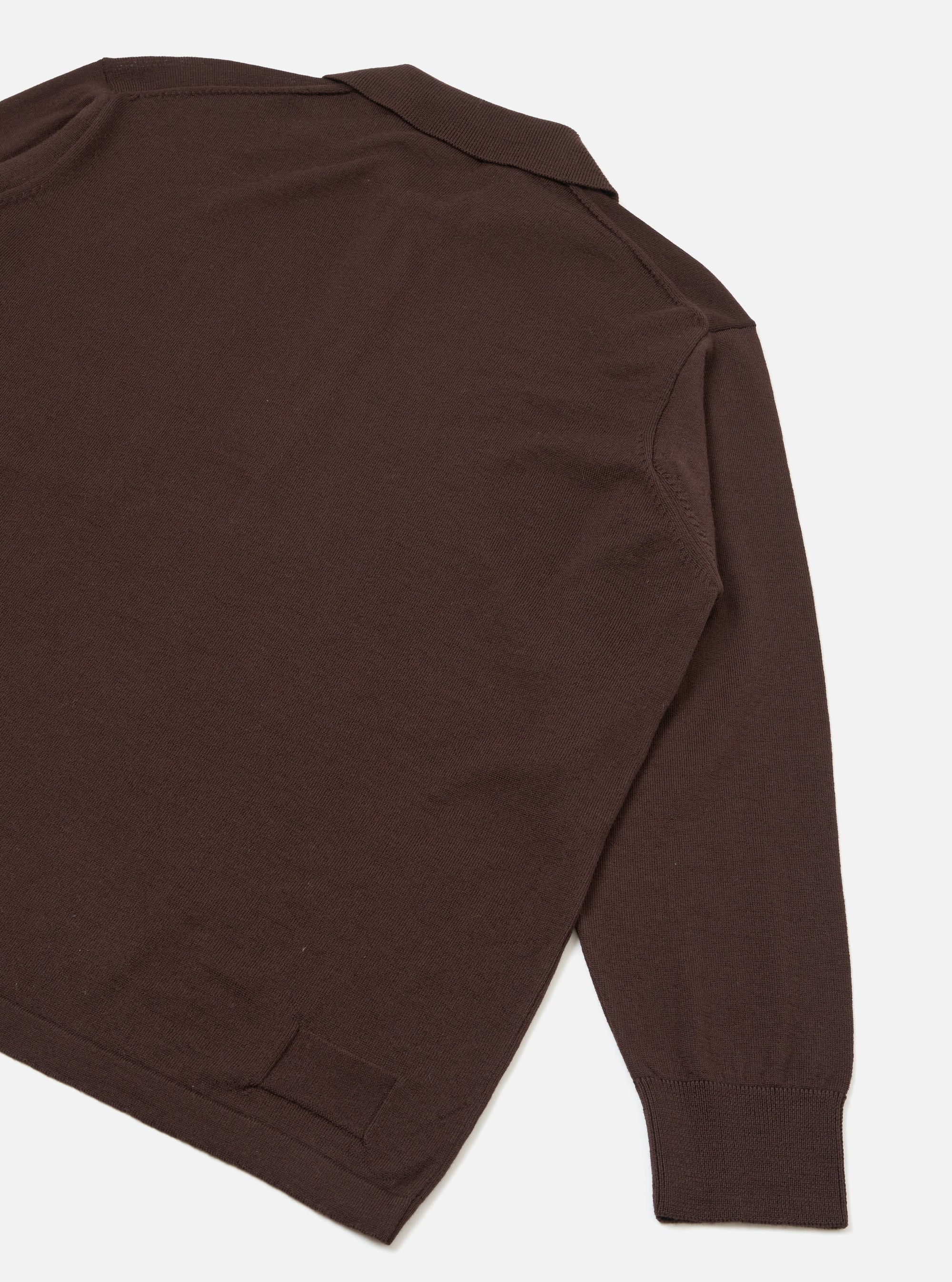 Flat lay detail shot of an espresso brown merino long-sleeve pullover knit shirt on a light grey seamless backdrop. The image shows the upper back, shoulder and one full sleeve. A ribbed polo collar is visible at the top, with a fine knit texture throughout. The cuff is ribbed and the hem has a clean ribbed finish.